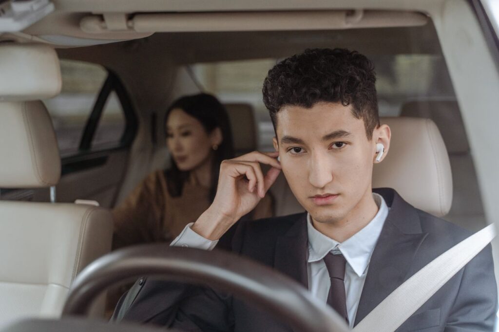 Crafting Captivating Headlines: Your awesome post title goes here A professional driver in a suit with AirPods driving a female passenger in a car.